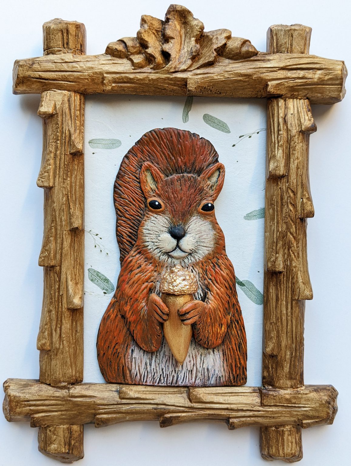 Gallery 6 - A clay squirrel holding a golden acorn in a frame topped with Oak leaves and acorns