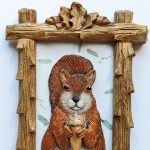 Gallery 6 - A clay squirrel holding a golden acorn in a frame topped with Oak leaves and acorns