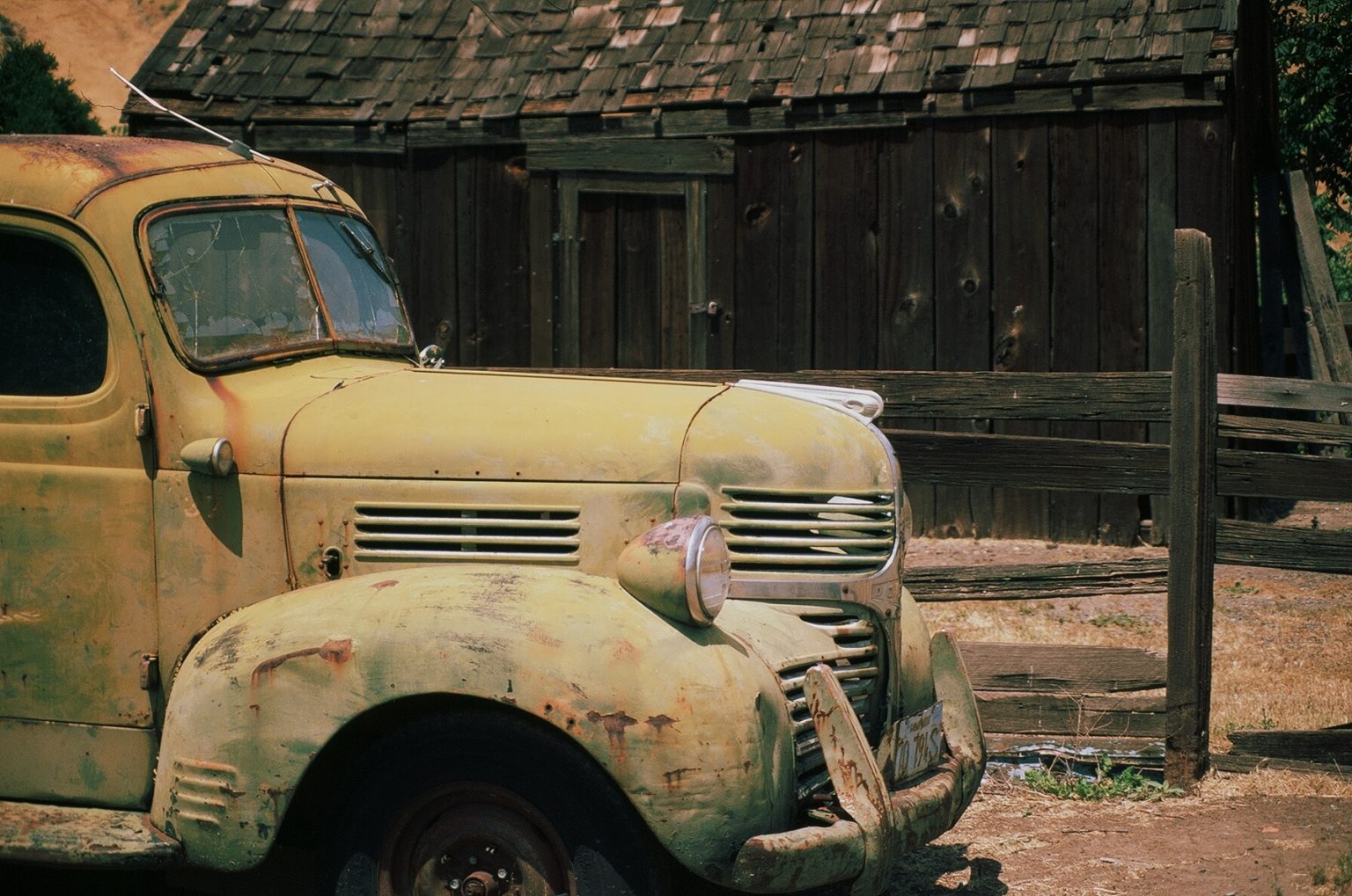 Gallery 3 - image of a rusty old yellow car on the left and an old wooden cabin on right side in the background