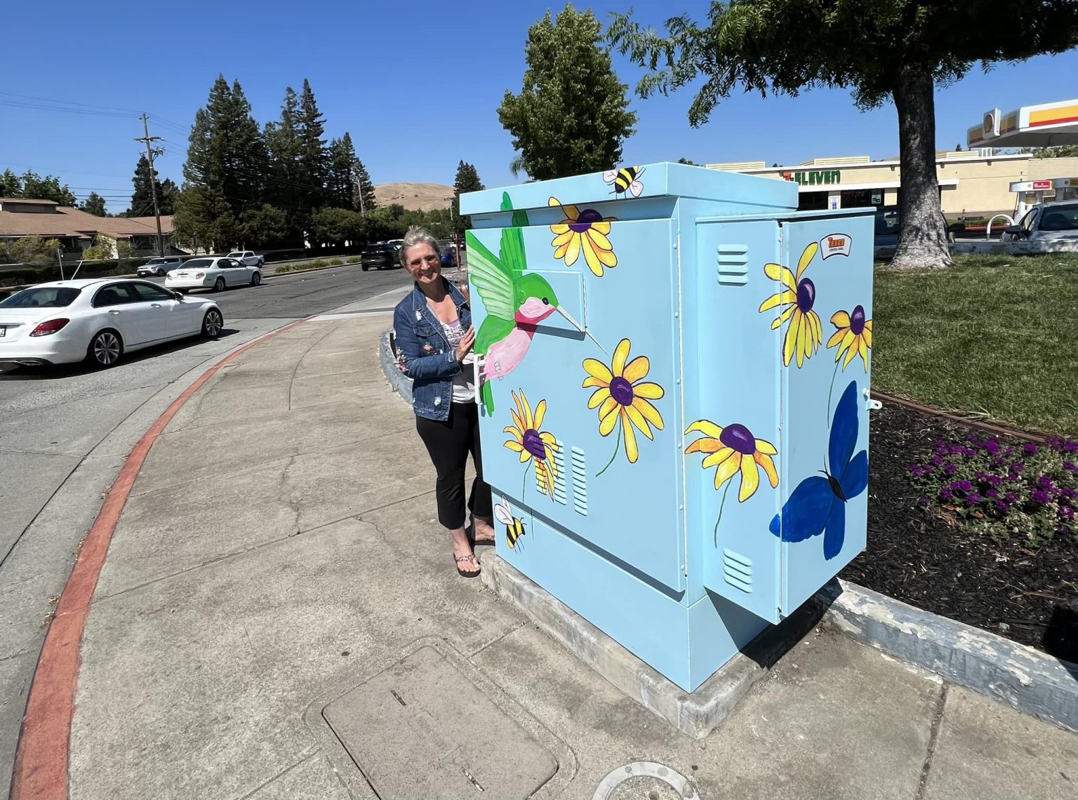 Gallery 1 - Picture of the artist to the left of the Utility Box Art on a sunny day