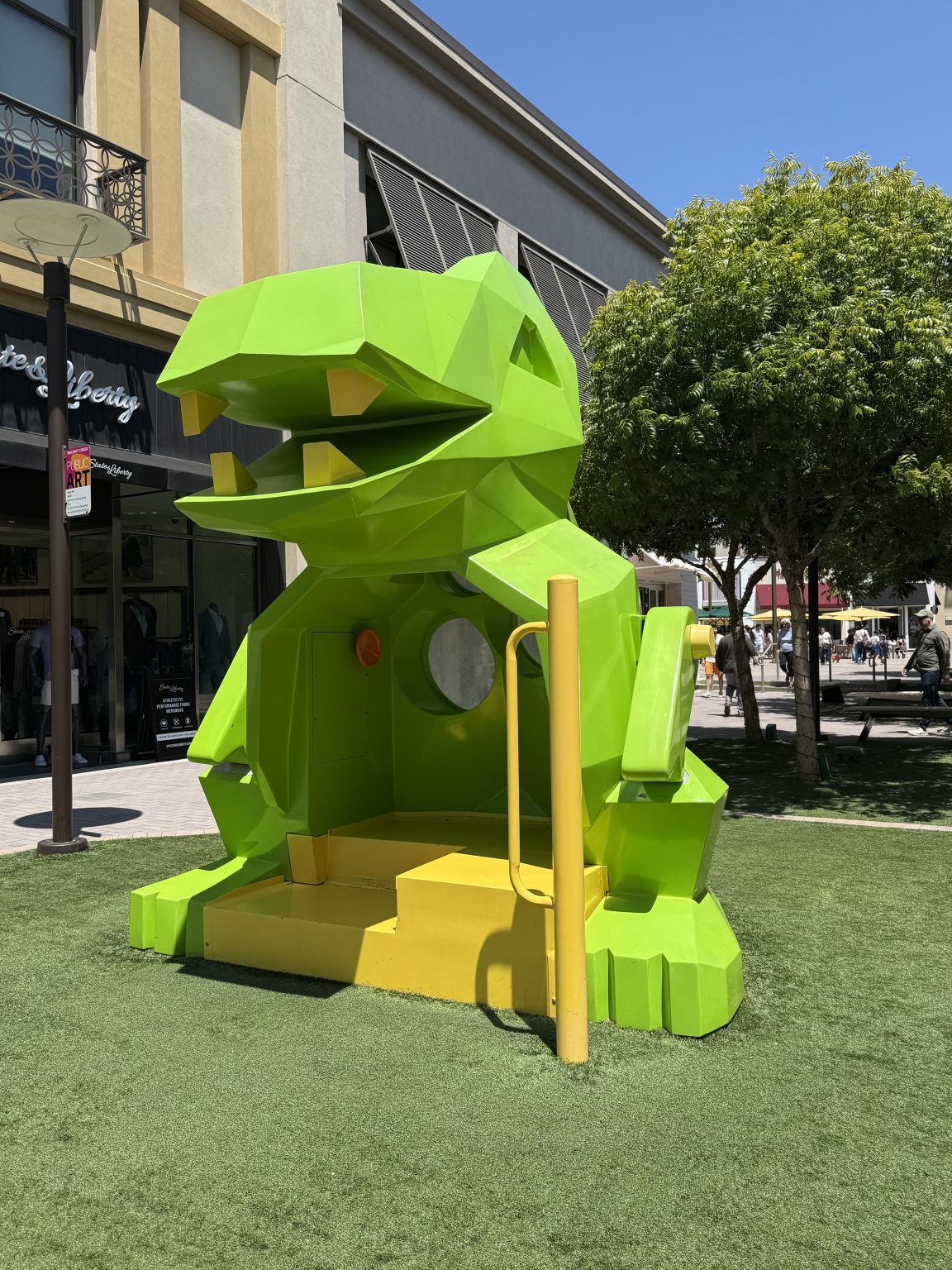 Gallery 2 - A large, faceted, green and yellow metal dinosaur-shaped seat for a children's playground.