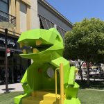 Gallery 2 - A large, faceted, green and yellow metal dinosaur-shaped seat for a children's playground.