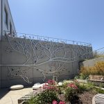 Gallery 9 - A 19-foot-high outdoor sculpture made of aluminum and illuminated with soft LED lights, featuring upward-reaching, branch-like forms inspired by the human nervous system and local plant life. A few large stone shaped benches in front of it.