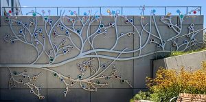 A 19-foot-high outdoor sculpture made of aluminum and illuminated with soft LED lights, featuring upward-reaching, branch-like forms inspired by the human nervous system and local plant life.