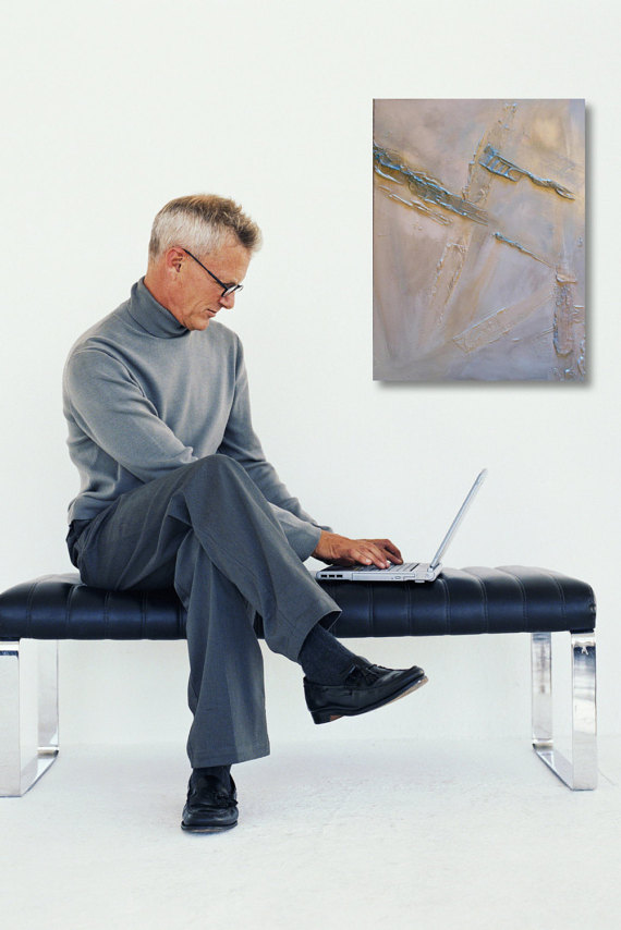 Gallery 6 - Older man in a gray turtleneck and trousers sitting on a black bench, using a laptop next to a muted abstract painting.