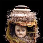 Gallery 6 - A dark and eerie mixed-media sculpture features a cracked baby doll head with blue eyes encased in an old, rusty lantern that is heavily decorated with dried moss and Spanish moss against a solid black background.
