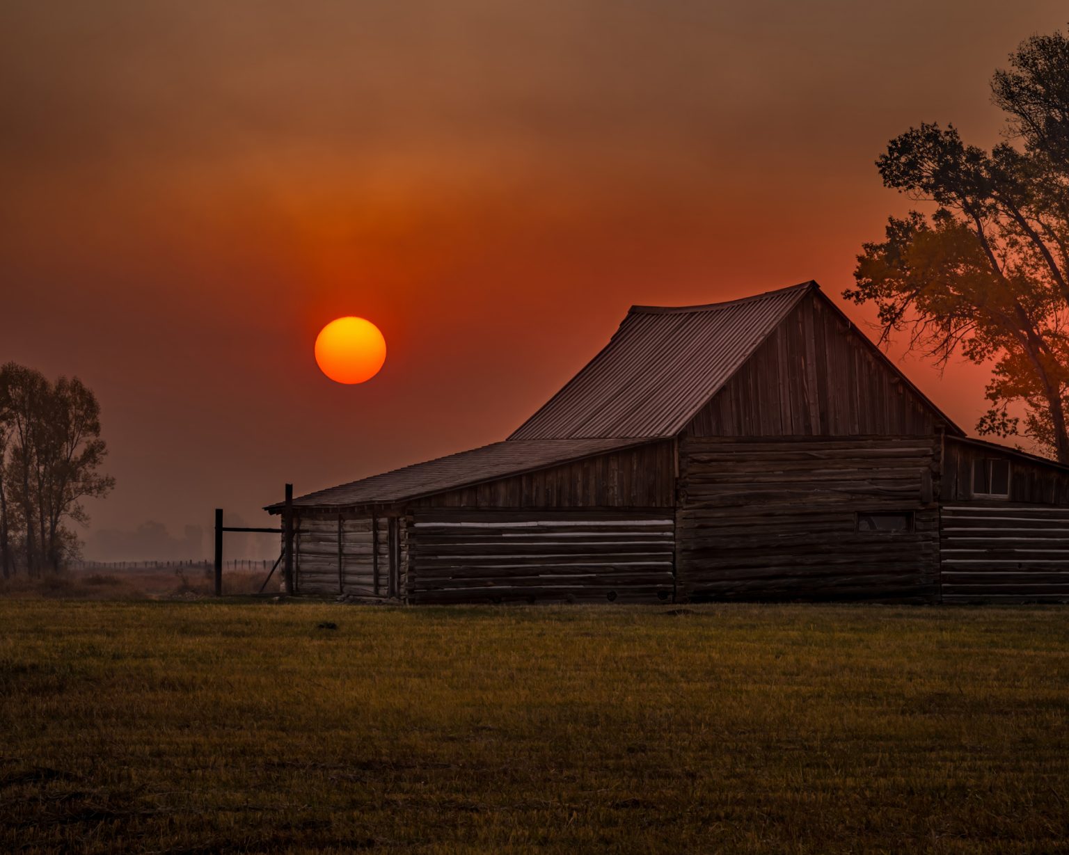 Gallery 10 - Picture of the iconic T.A. Moulton Barn in Grand Teton NP with the sun rising through thick smoke.