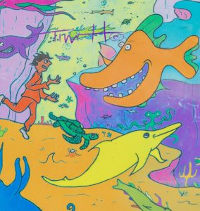 A brightly colored, cartoon-style mural on a rectangular Bigbelly trash bin showing a human figure swimming among numerous smiling and whimsical sea creatures, including a large orange fish and an octopus playing a golden harp.