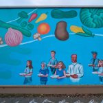 Gallery 4 - Mural on a wall with a blue background and people holding empty plates, and there are floating vegetables at the top.