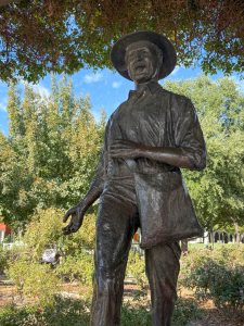 A bronze statue of a man with a bag scatters seeds in a park.