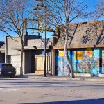 Gallery 1 - A wide, multi-panel mural wrapping around a building featuring colorful figures, portraits, and geometric patterns. Sections include a portrait of Bayard Rustin, a cyclist, a woman flexing, and vibrant rainbows and sunflowers.