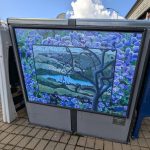 Gallery 3 - A utility box features a landscape painting of the San Pablo Reservoir viewed through the branches of a dark, twisting tree. The central image is framed by a dense border of vibrant purple hydrangeas, and a small plaque encourages viewers to find six hidden animals.