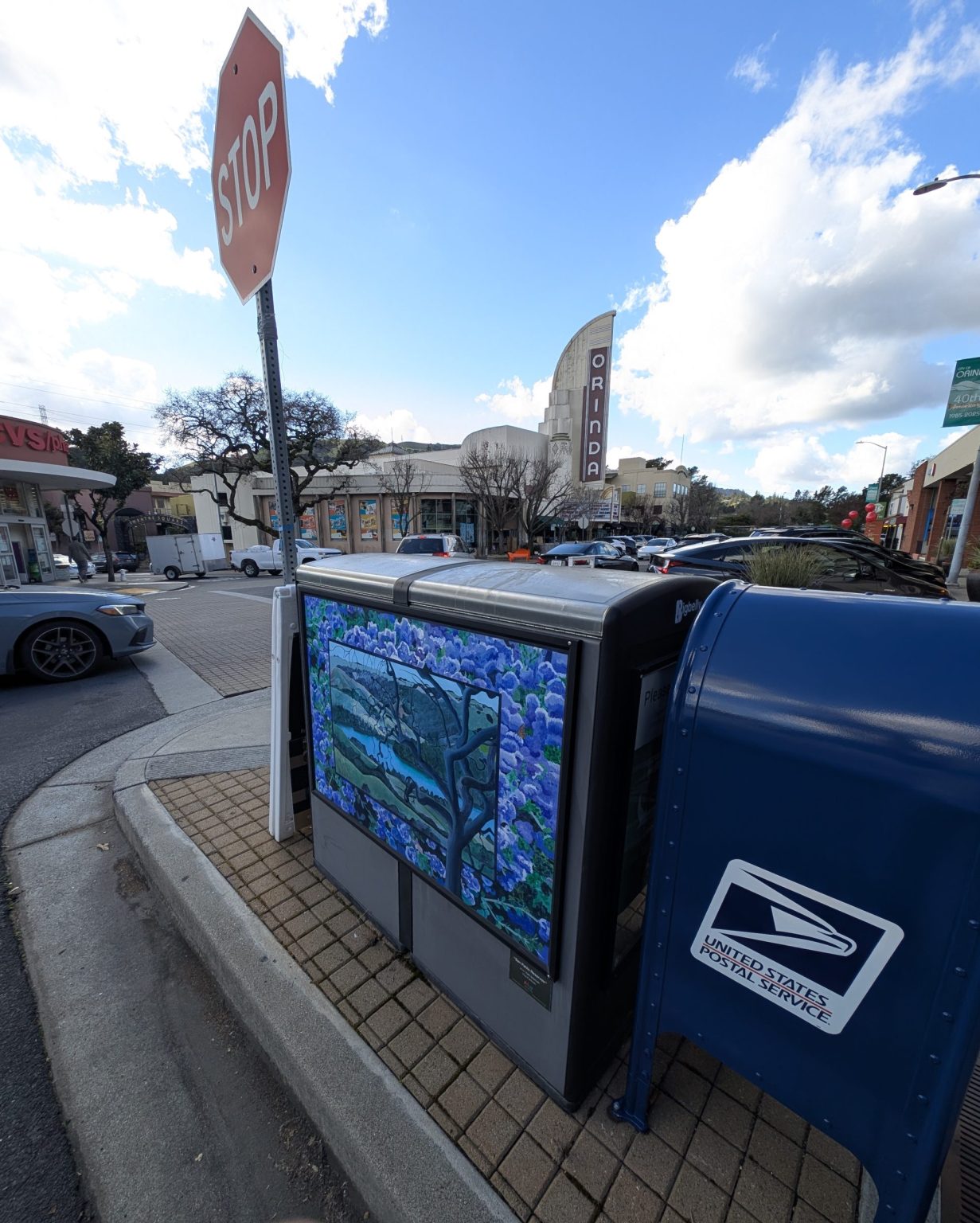 Gallery 4 - A utility box features a landscape painting of the San Pablo Reservoir viewed through the branches of a dark, twisting tree. The central image is framed by a dense border of vibrant purple hydrangeas, and a small plaque encourages viewers to find six hidden animals.
