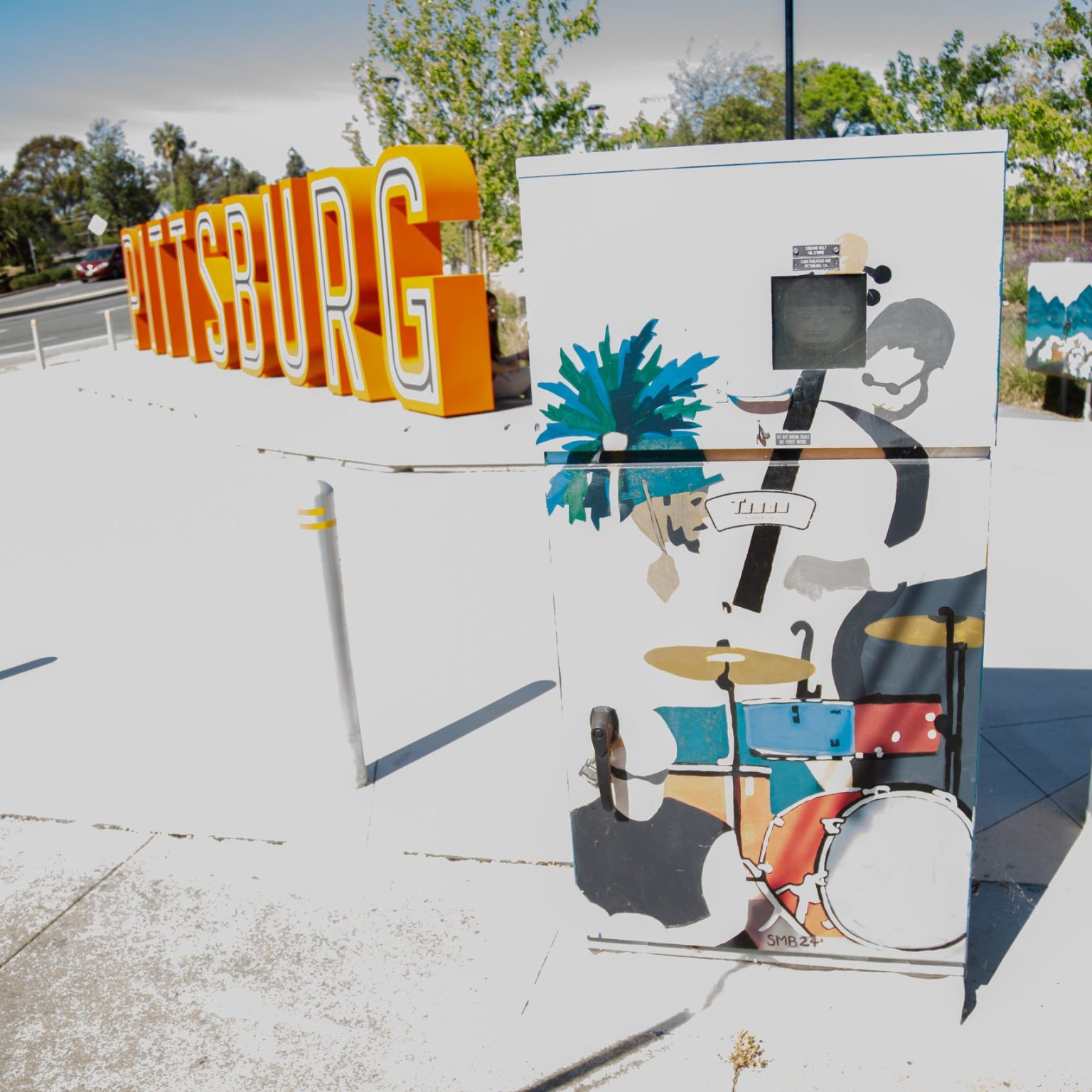 Gallery 1 - A series of three utility boxes painted with colorful murals. One box shows a classic black car with 