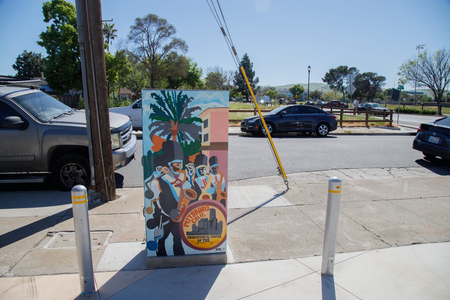 Gallery 5 - A series of three utility boxes painted with colorful murals. One box shows a classic black car with 