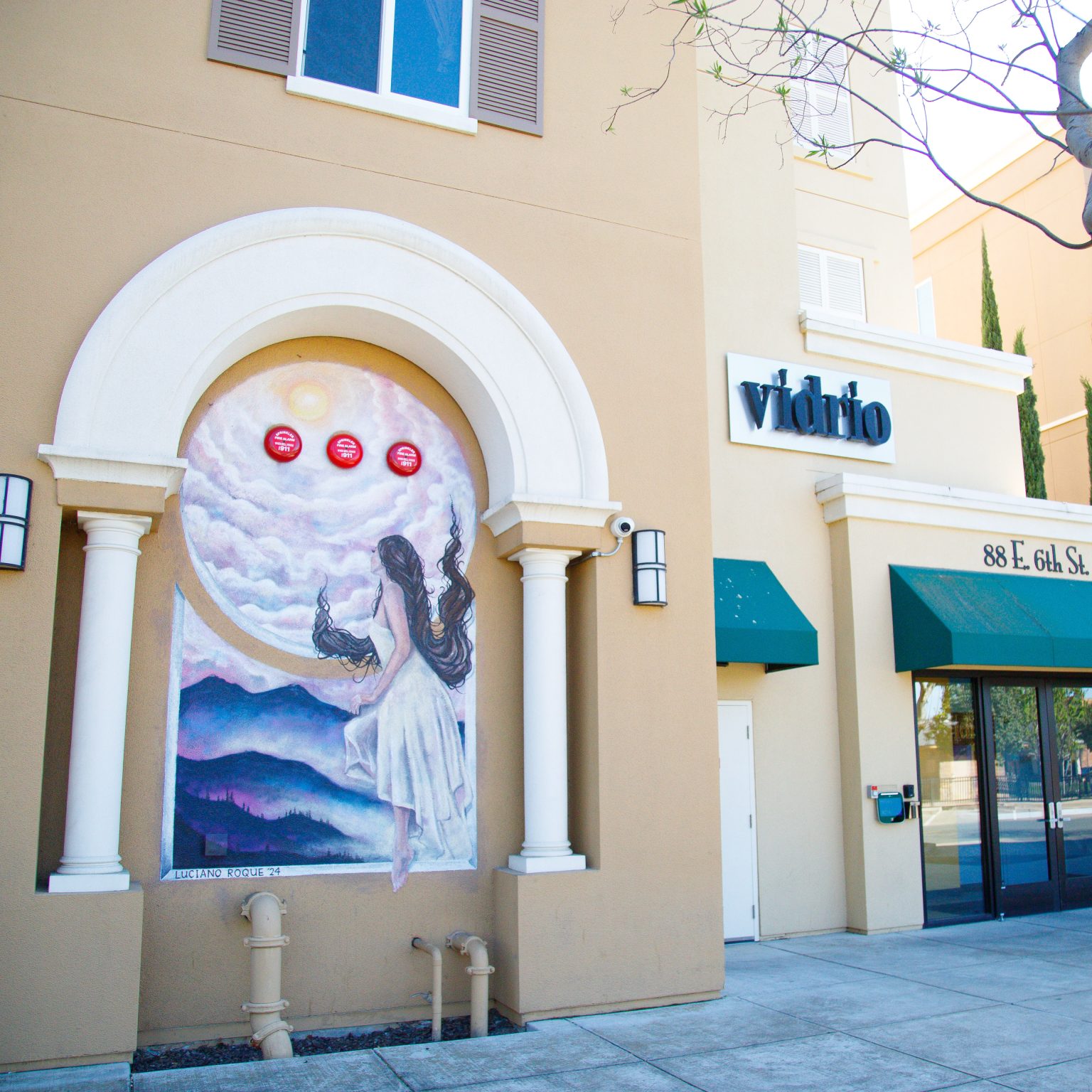 Gallery 1 - A large-scale mural on the side of a commercial building featuring bold, colorful portraiture blended with geometric shapes and flora. The composition uses a warm palette of oranges and teals to highlight the intersection of the city's industrial heritage and its community growth.