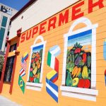 Gallery 1 - Alt Text: A painted mural on an orange cinder block wall displays the word 