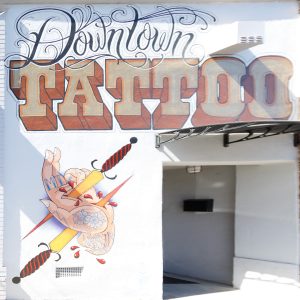 A photograph of the building facade at 710 Las Juntas Street in Martinez, California, showing a painted "Downtown Tattoo" storefront sign and dagger-pierced heart mural next to an Aladdin Bail Bonds entrance.