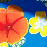Gallery 3 - A vibrant painted utility box featuring a pink hummingbird in flight against a bright blue sky, surrounded by orange fruit and small white blossoms, with text reading 